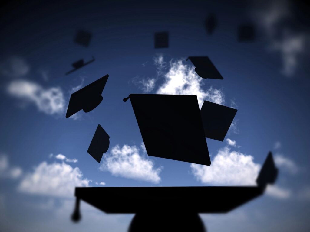 Graduation hats in the air against sky and clouds